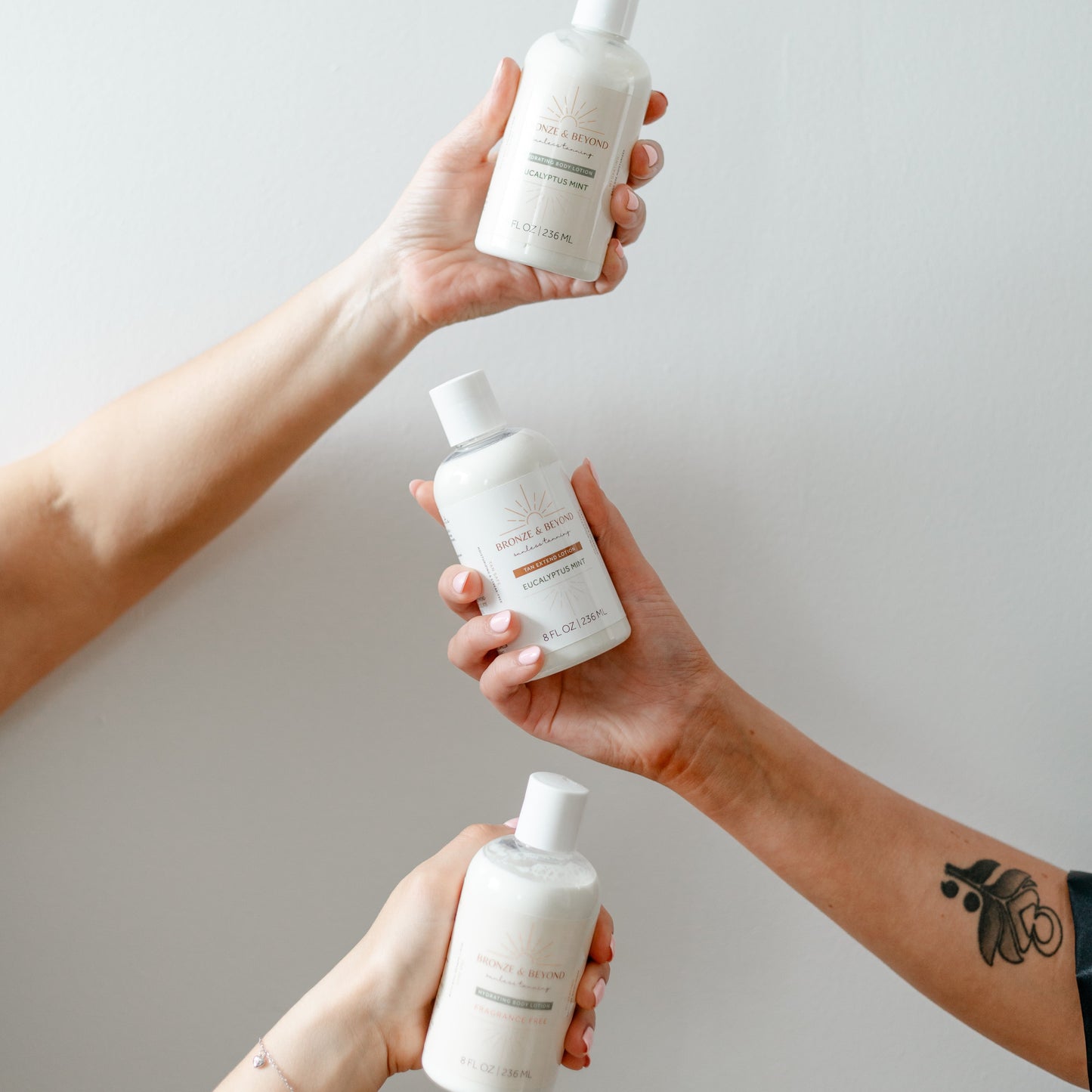 Three hands holding white bottles against a plain background