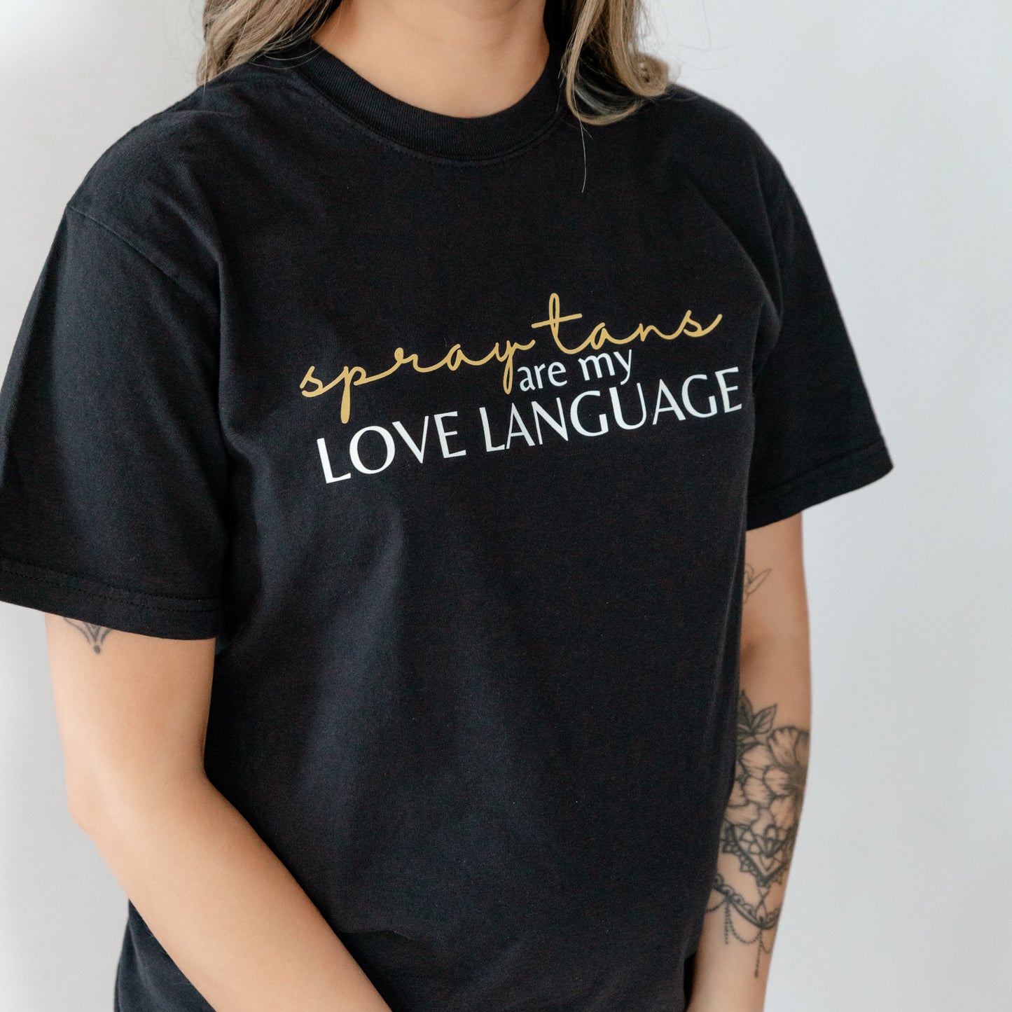 woman wearing a black shirt that says "spray tans are my love language"