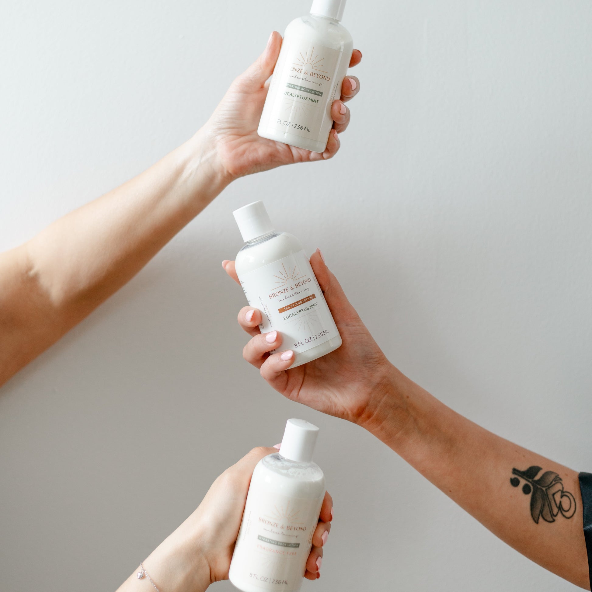 Three hands holding white bottles against a plain background