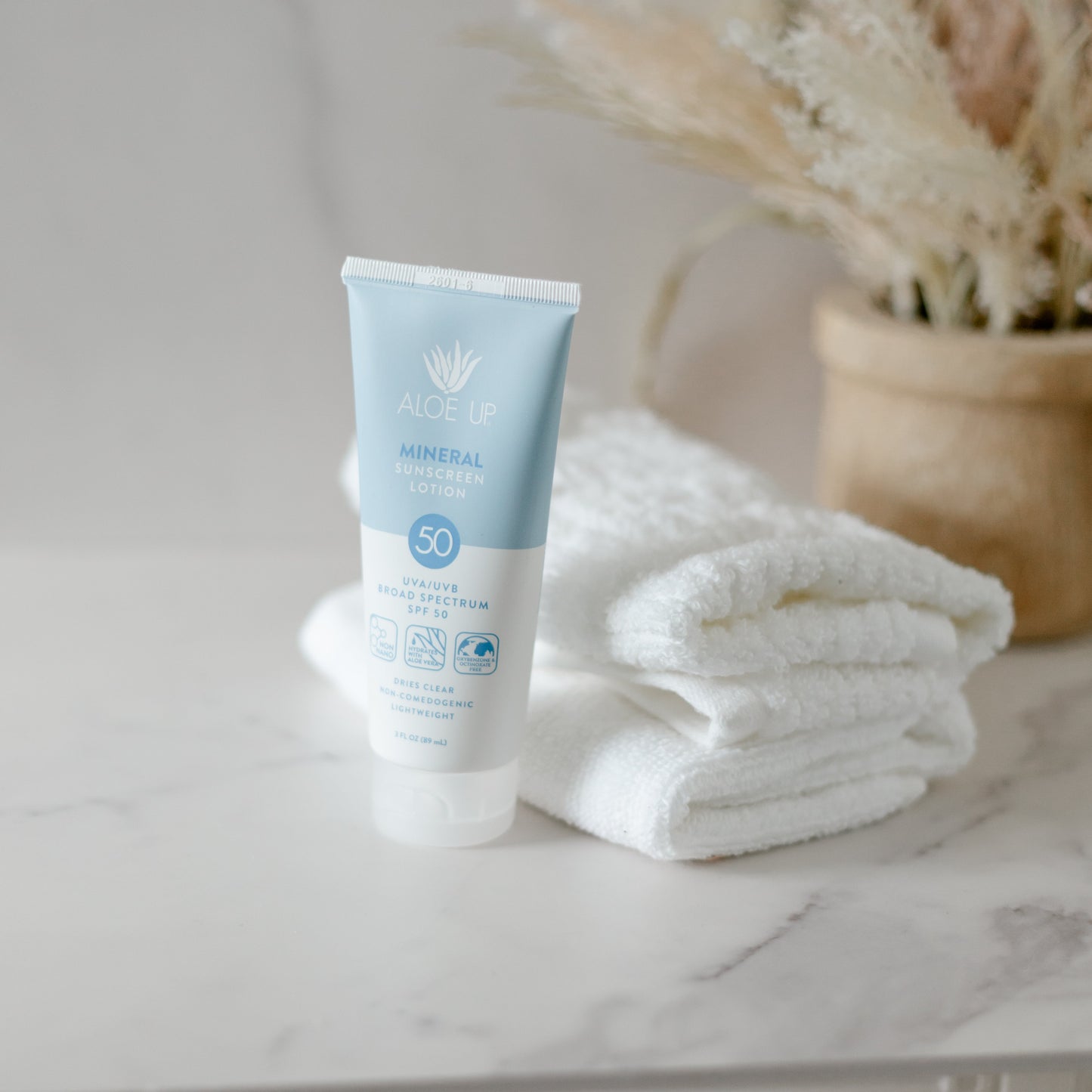 Tube of spray tan safe sunscreen on a marble surface with a decorative plant in the background